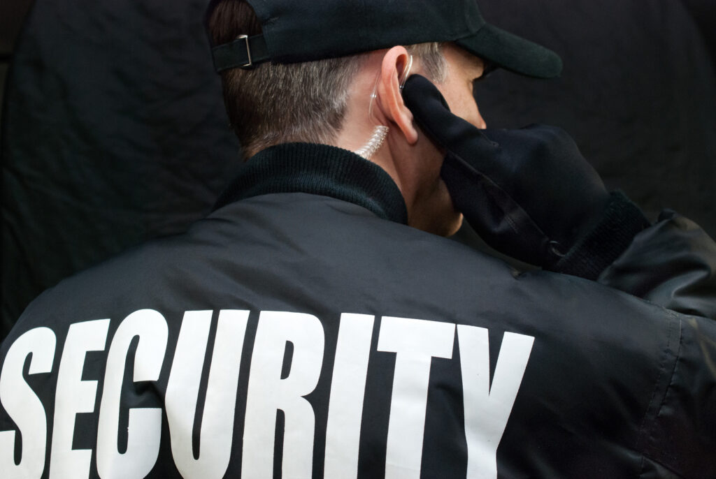 Armed Security Guard Listens To Earpiece, Back of Jacket Showing Los Angeles CA, Chino Hills CA,